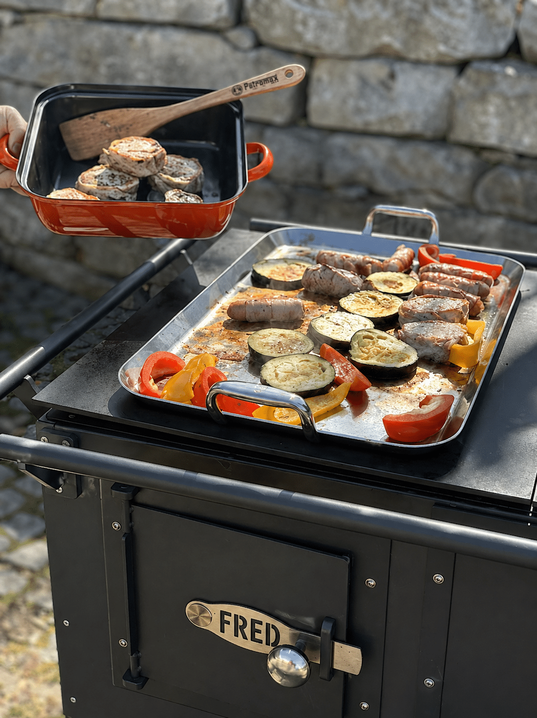 fred_schwarz5 174 Im Freien wird gegrillt: Würstchen, Zucchinischeiben und Paprika werden auf einem Metallblech gegart; in einer roten Pfanne wird über dem Grill mit einem Holzspatel geschnittenes Brot geröstet.